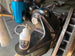 Sure-Lock 30ml white bottle by Revlock Race Supplies; two items: white bottle and blue anodized fitting in workshop.