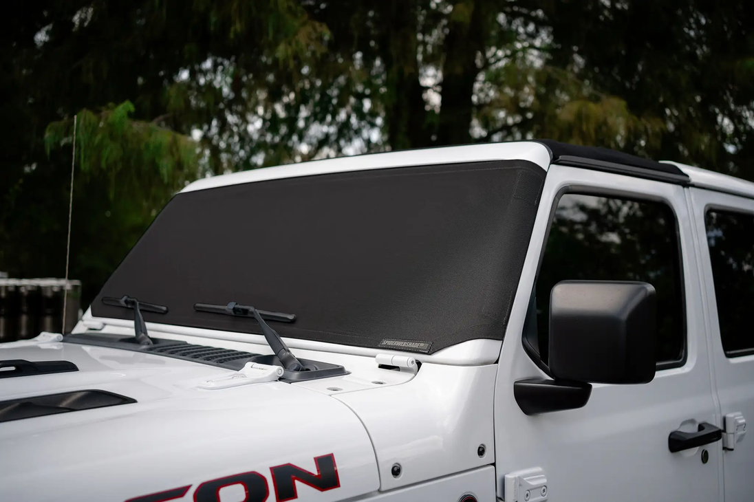 Solar shade for Jeep Wrangler/Gladiator by SpiderWebShade on white SUV; black mesh with brand badge.