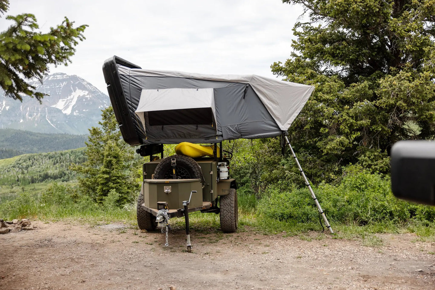 Smittybilt Overland X L hard shell tent mounted on roof rack of rugged off-road vehicle; gray with white panels