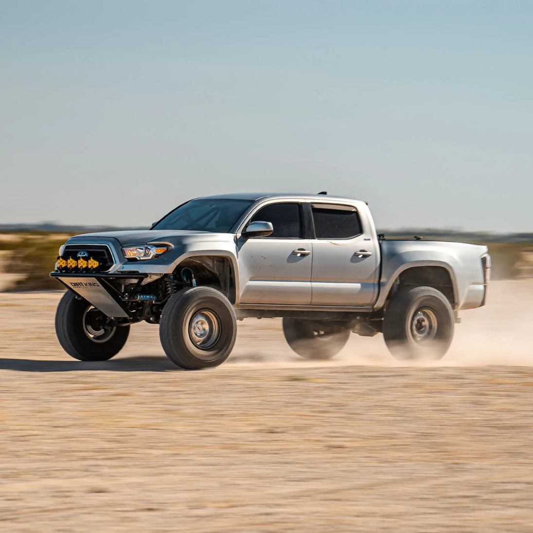Long Travel Kit Dirt King Toyota pickup white with aftermarket front bumper and yellow LED lights
