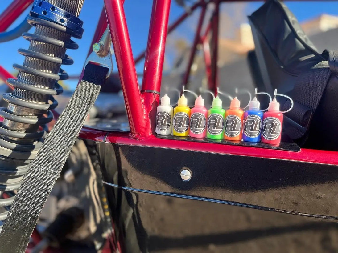 Sure-Lock 30ml bottles by Revlock Race Supplies (RL) in rainbow colors lined on a red motorcycle frame, nine bottles.
