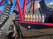 Sure-Lock 30ml bottles by Revlock Race Supplies (RL) in rainbow colors lined on a red motorcycle frame, nine bottles.